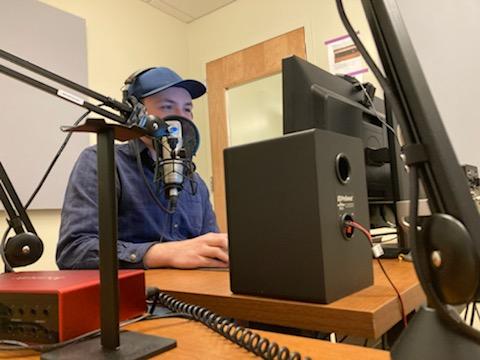 The author Austin Shaffer sitting behind a microphone and other recording equipment at the University of Wyoming's Studio Coe.
