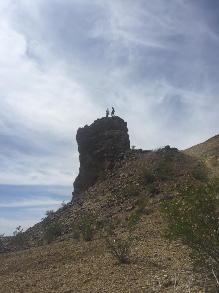 Two people standing atop a boulder set on a hill